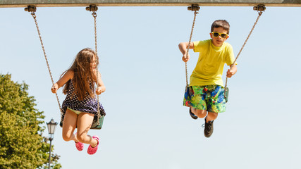 Two children having fun on swingset. - obrazy, fototapety, plakaty