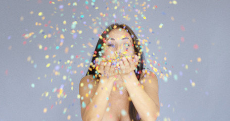 Young woman blowing colorful New Year confetti off the palms of her hands as she celebrates the...