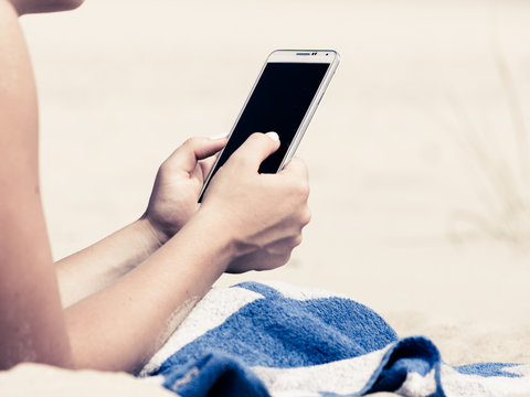 Woman on beach texting on smartphone.