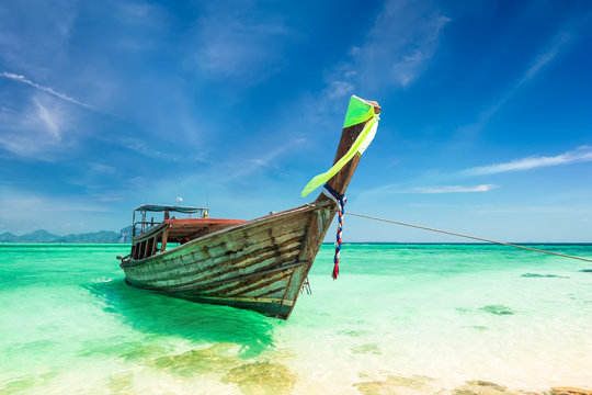 Thai traditional wooden boat with ribbon decoration at ocean shore under blue sky.Thailand tropical beach landscape