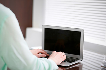 Business woman hands in a green blouse sitting at the desk in the office and typing on the laptop .