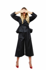 Sexy blonde young woman in fancy dark clothes holding her hands to eyes isolated on white