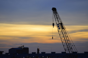Construction site, silhouettes of construction industry , Crane and building refinery plant construction site against sunset .