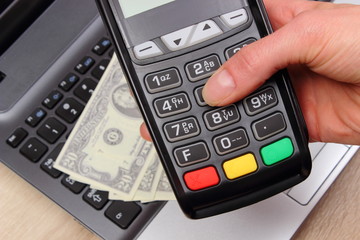 Fototapeta premium Hand of woman using payment terminal, currencies dollar on laptop in background