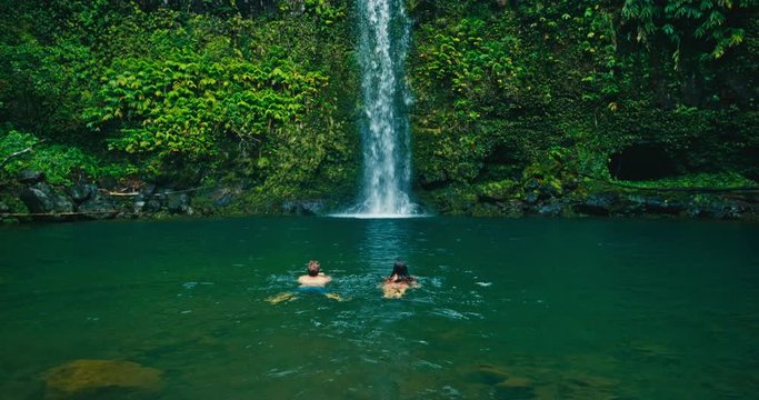 Attractive adventurous young couple swimming to beautiful waterfall
