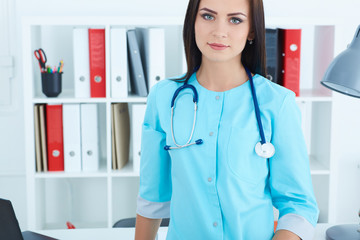 Beautiful confident female medicine doctor standing in her office looking in camera. Medical help or insurance concept.