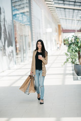 Attractive cute girl in with the shopping bags and warm drink in her hand