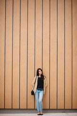 Stylish beautiful woman smiling stands near a wooden wall.