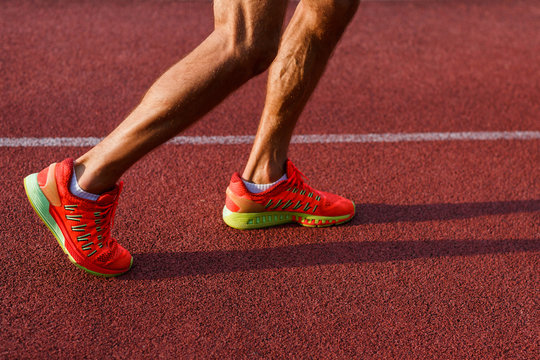 Muscular legs of man in sneakers on running track