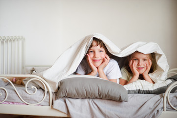 Little brother and sister made a play on the bed in the bedroom.