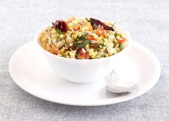 Kosambari, a traditional and popular, south Indian salad made from split mung bean, lentil, cucumber and other items, in a bowl on a plate with a steel spoon.