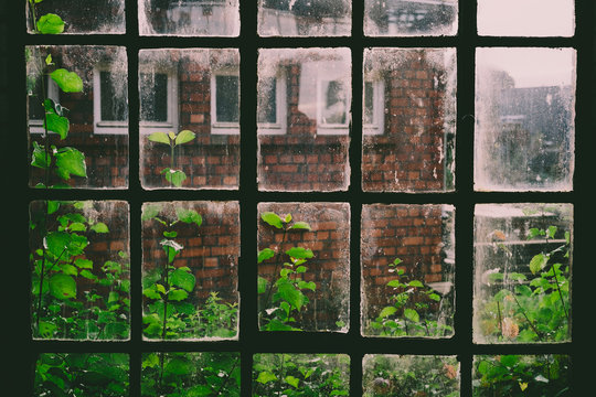 Altes Sprossenfenster in einer historischen Werkshalle mit Ausblick auf ein historisches Fabrikgebäude aus Backstein.