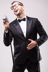 Naklejka premium Young man in suit singing over the microphone with energy. Isolated on white background. Singer concept.