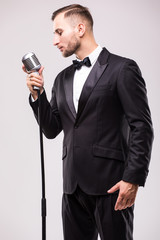 Naklejka premium portrait of young man in suit singing with the microphone. Isolated on grey background. Singer concept.