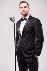 Naklejka premium portrait of young man in suit singing with the microphone. Isolated on grey background. Singer concept.