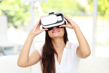 Young woman wearing virtual reality glasses and sitting on sofa on blurred background