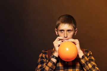 Young man puffing balloon on dark background © Africa Studio