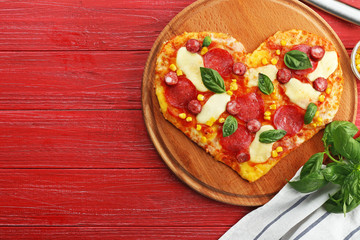Plate with heart-shaped pizza and its ingredients on wooden background