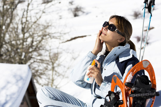femme assise dans la neige s'appliquant de l'&eacute;cran de protection sur le visage