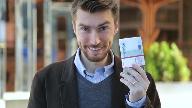 Attractive man leafing through a bundle of euros, looking at camera and smiling