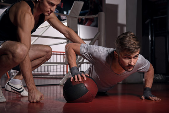 Man doing push-ups with trainer using fitness ball - Powered by Adobe