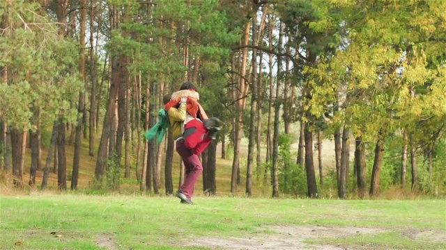 Guy picks up girl on hands and circling her in woods. Man with woman walks in forest. Young couple is spending time together. Best moments of life