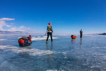 Fototapeta na wymiar a woman and a man with a sledge and trekking pole is ice of Baik