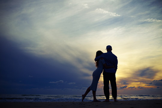 Silhouette of couple embracing while looking to the sunset
