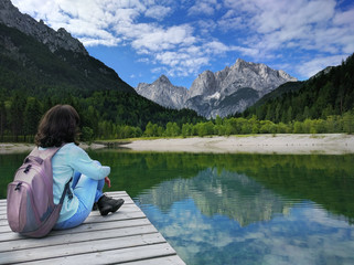 View of the Julian Alps with girl sitting on pier in Slovenia