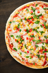 Pizza with mozzarella cheese, chicken, sweet corn, sweet pepper and parsley on dark wooden background top view. Italian cuisine.