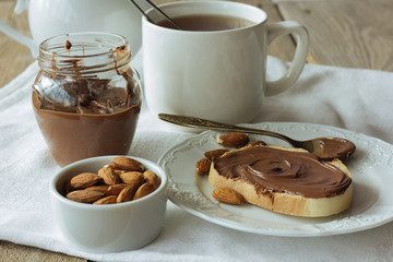 Piece of bread with chocolate paste, cup of tea and almonds