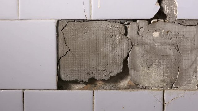 Interior of an old house cracked ceramic tiles falling off from the wall in the bathroom or kitchen closeup dolly shot