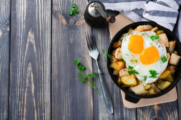 Hearty breakfast. Hash brown potatoes, chicken, onion, parsley, oregano and a fried egg in a frying pan on the old wooden background. Top viewSelective focus.