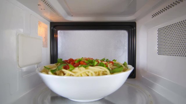 Bowl of cooked spaghetti with tomato sauce heating in the microwave oven pasta dish rotates on turntable plate inside view