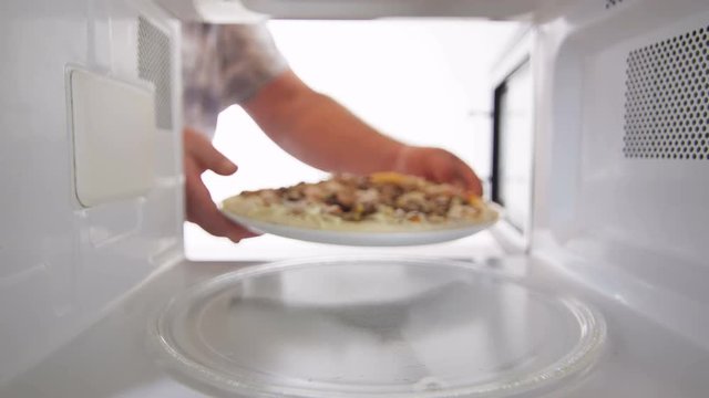 Defrosting frozen seafood pizza Frutti di Mare in microwave man putting dinner into the oven. Inside view version with external lighting