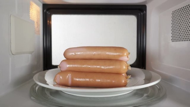 Cooking sausages in the microwave. Heap of  sausages on a plate rotates on turntable inside oven.