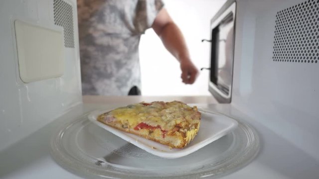 Reheating leftover slice of pizza in microwave man putting plastic plate with pizza in the oven