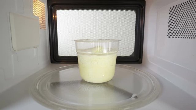 Container with frozen cheese soup warming up in the microwave oven