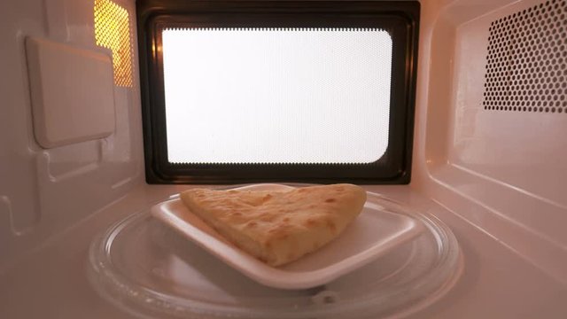 Plastic plate with slice of cheese pie spinning on turntable in the microwave oven. Version without external lighting for more natural look. 