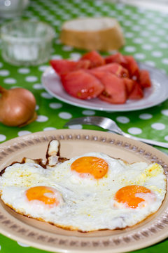 Fried eggs for breakfast with tomato in background