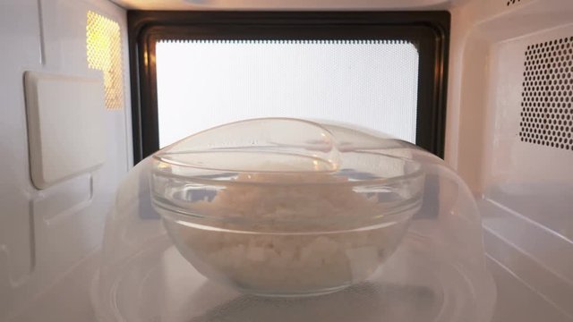 Cooked white rice covered with plastic plate cover heating in the microwave oven