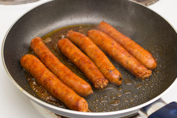Frying homemade red sausages in frying pan
