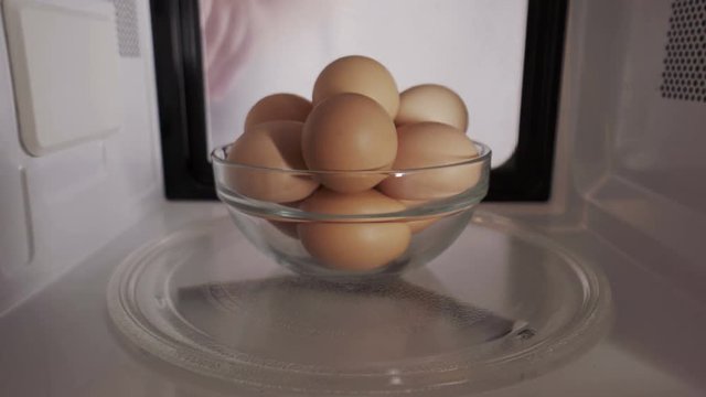 Man puts chicken brown shell eggs inside microwave oven and turns it on. Cooking eggs in the shell in a microwave is very dangerous and may cause the eggs to explode.