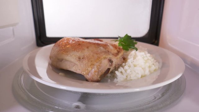 Pan fried chicken leg with rice on a plate reheating in the microwave oven before serving. Version with external lighting