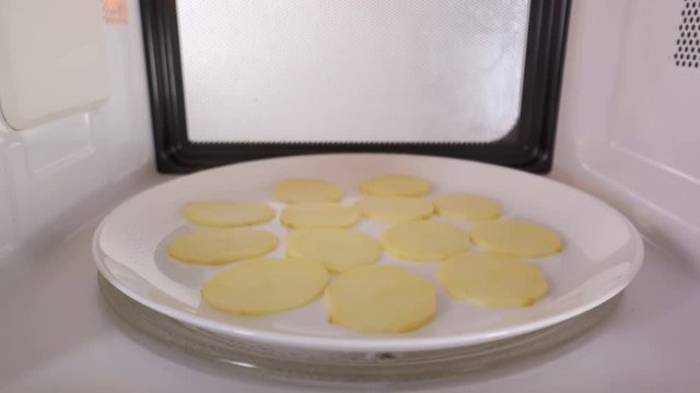 Homemade baked potato chips cooking in the microwave oven. Potato slices on a plate baking inside microwave