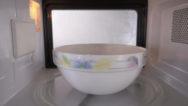 Ceramic bowl with some food heats up in the microwave spinning on turntable tray inside oven