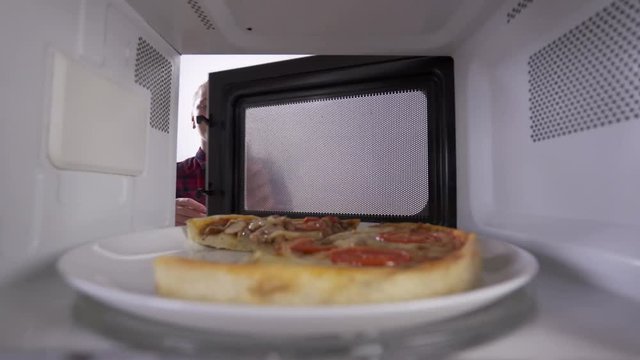 Reheating leftover pizza in the microwave. Young girl opens the door and takes out slice of heated pizza. View through the oven.
