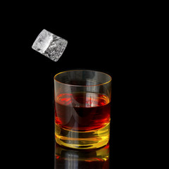 Isolated shot of whiskey with falling ice on black background.
