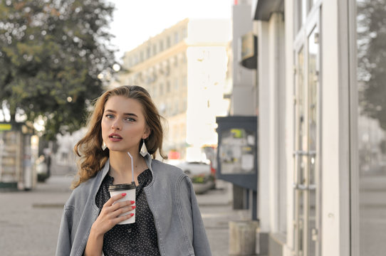 Girl goes on the sidewalk and drinking coffee