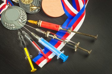 Syringe and medals. Doping in sport. Abuse of anabolic steroids for sports. Anabolic steroids spilled on a wooden table. Fraud in sports. Doping athletes.
